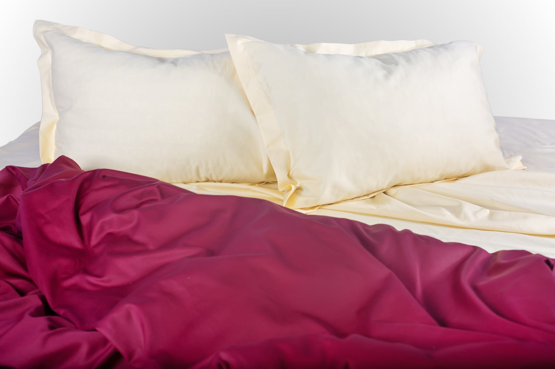 Styled cream and burgundy sateen bed linen by Once@Home creating a warm and refined bedroom atmosphere