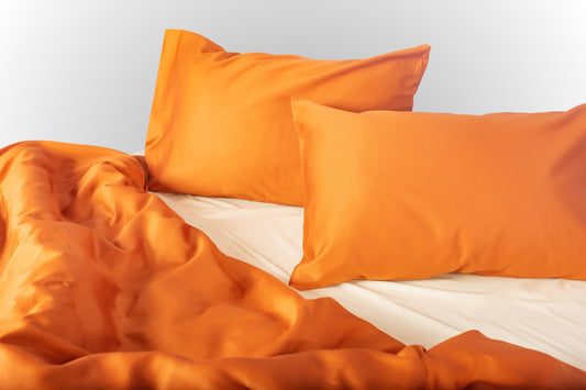 Close-up of terracotta-cream sateen bed linen by Once@Home showing gentle folds and refined finish